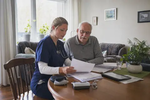 „Häusliche Krankenpflege – Antrag“: Eine Pflegefachperson bespricht mit einer pflegebedürftigen Person die weitere Versorgung nach einer Behandlung.