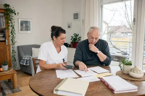 „Häusliche Krankenpflege – Kosten“: Eine Pflegefachperson bespricht mit einer pflegebedürftigen Person die weitere Versorgung nach einer Behandlung.