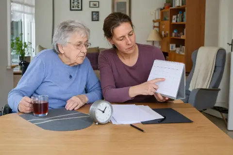 Pflegetagebuch für die Begutachtung – Fristen „Pflegetagebuch für die Begutachtung – Fristen“: Eine Angehörige und eine pflegebedürftige Person prüfen gemeinsam Pflegeunterlagen an einem Tisch.