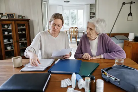 „Pflegeunterstützungsgeld – Unterlagen“: Eine pflegende Angehörige prüft Unterlagen zur Vereinbarkeit von Beruf, Absicherung und Pflege.